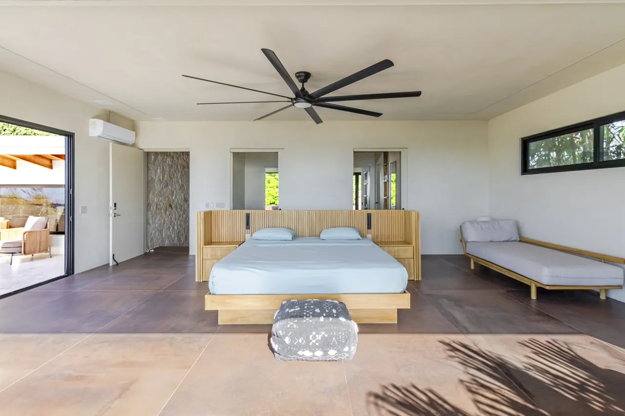 Spacious king bedroom with timber headboard, ceiling fan and upholstered bench