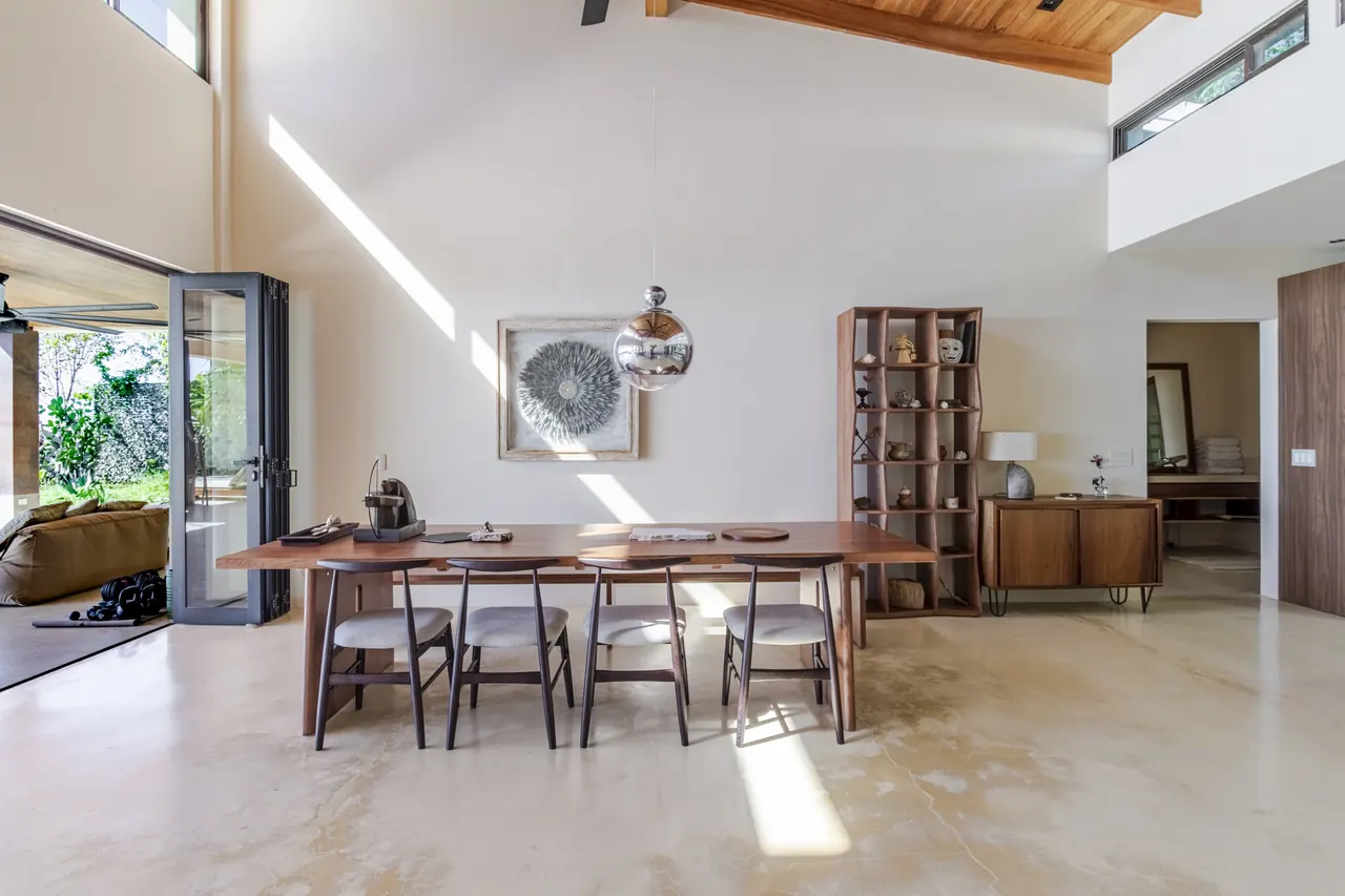 Long timber dining table beside open shelving and the living area