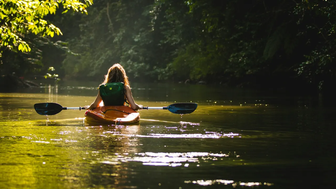 A kayaker paddles through a green, forest-lined waterway in the Drake Bay area.