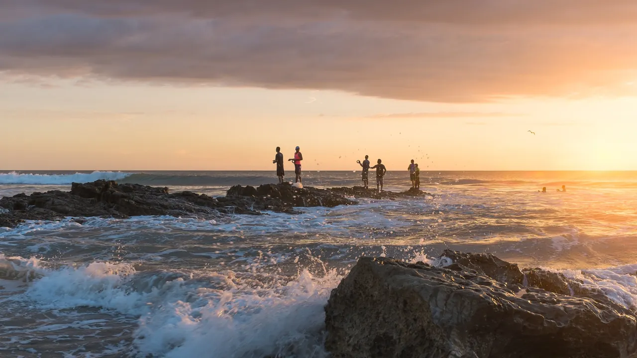 People fishing from a rocky shoreline at sunset on Playa Santa Teresa.
