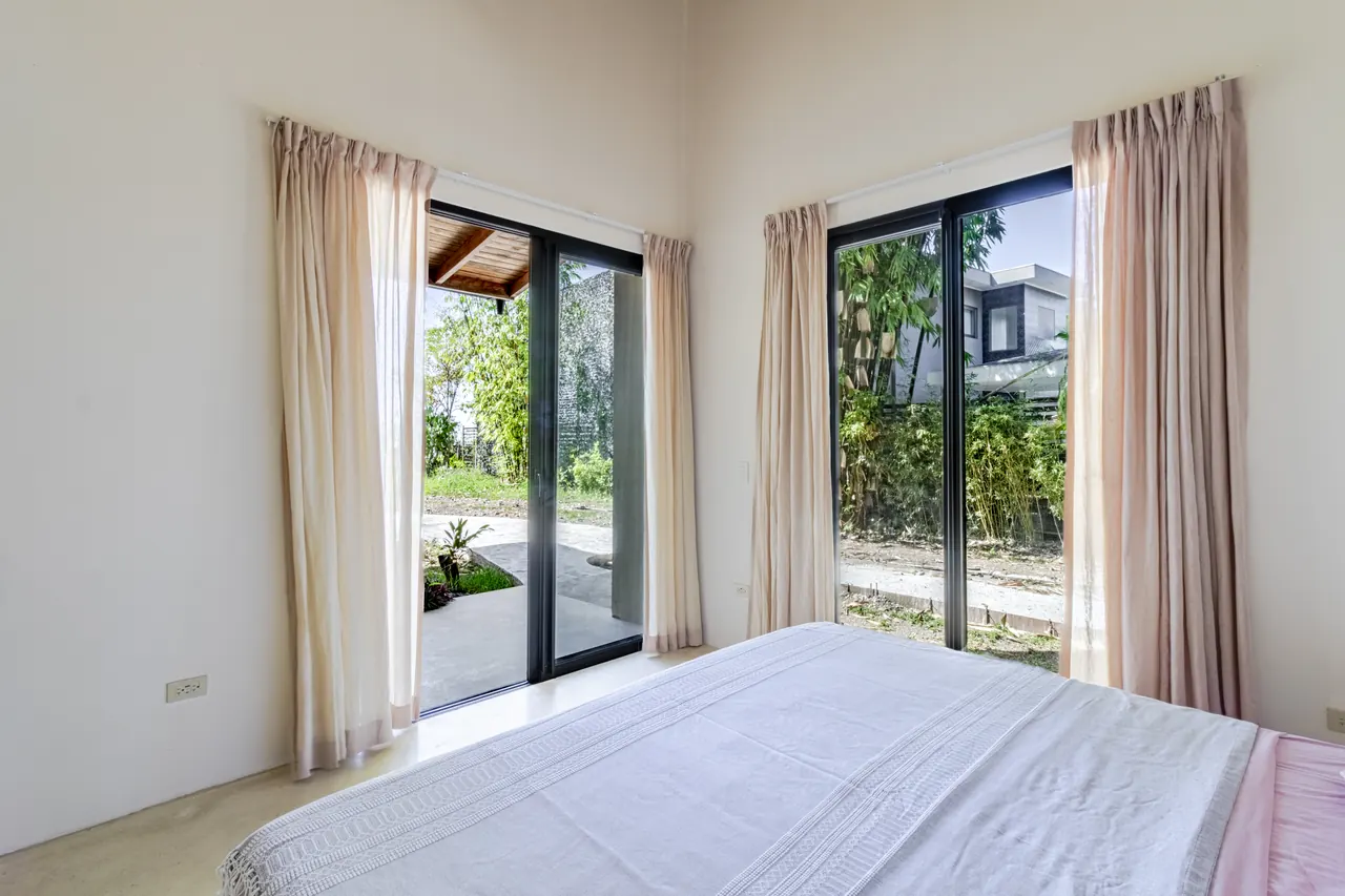 King bedroom with soft curtains and corner windows toward the garden