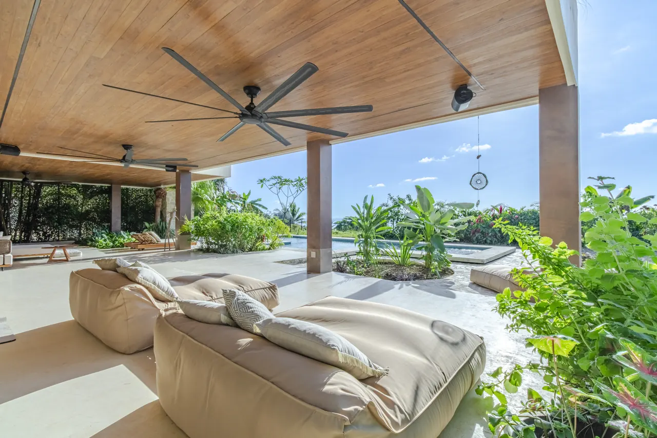Deep terrace sofas beneath a timber ceiling beside tropical planting